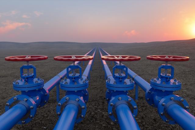 Blue oil or natural gas pipeline stretching across a landscape of soil at sunset, with red-handled valves in the foreground