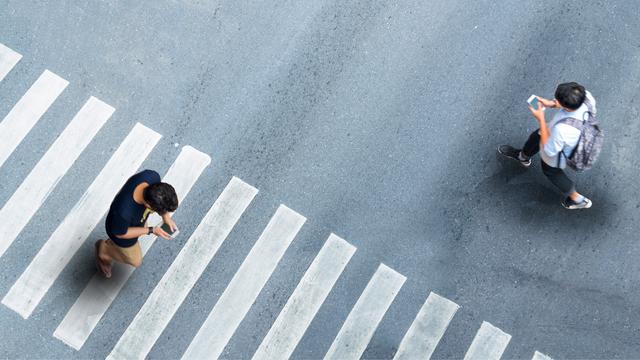 Aerial top view of two people in a crosswalk looking at their phones as they walk