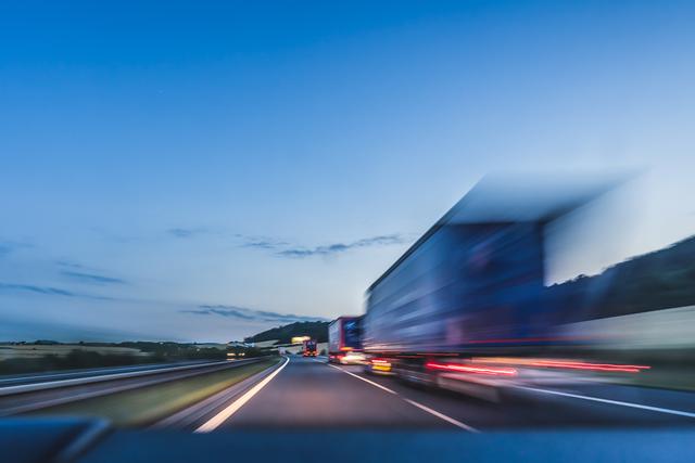 Trucks traveling on a highway at dusk or dawn, with motion blur and light trails